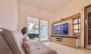 Ett modernt vardagsrum med en stor TV med platt skärm, en soffa och en skjutdörr i glas som leder ut till ett utomhusområde.