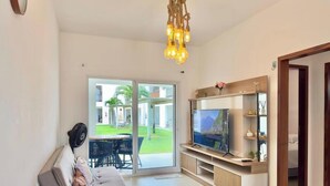 Sala de estar con televisión, sofá, ventilador y vista a un jardín a través de un ventanal corredero.