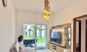 A living room with a TV, a sofa, a fan, and a view of a garden through a sliding door. - (Aracati)