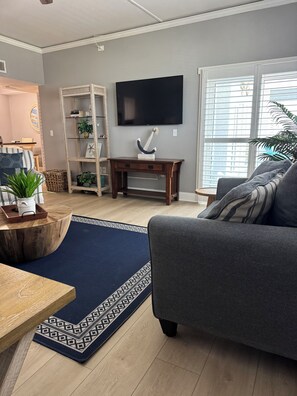 A living room with a grey sofa, a wooden coffee table, a blue patterned rug, a wooden side table, a TV on the wall, and a bookshelf with decorative items. - Beachfront Bliss at San Remo
Stunning Redington Shores Condo on Gulf Blvd. (Redington Shores)