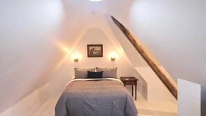 Una camera da letto con soffitto spiovente, un letto con lenzuola a righe, due luci a parete e un quadro incorniciato.