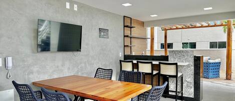 Un espacio interior moderno con una mesa y sillas de madera, un televisor de pantalla plana y una cocina integrada.