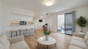 A modern living room with a marble coffee table, a sofa, and a kitchen area with a TV and bar stools. - Quiet Lakefront Home with Boat, Hot Tub, Game Room, Great Views, Sleeps 10 (Gilbert)