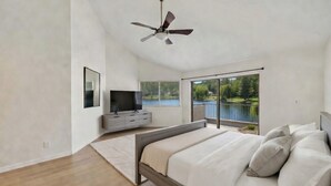 A bedroom with a bed, a television, a ceiling fan, and a large window with a view of a lake. - Quiet Lakefront Home with Boat, Hot Tub, Game Room, Great Views, Sleeps 10 (Gilbert)