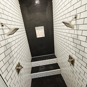 A narrow, tiled shower with black and white tiles, a small window, and a showerhead on the wall. - Unique +Upscale +4 Bedroom (Shreveport)