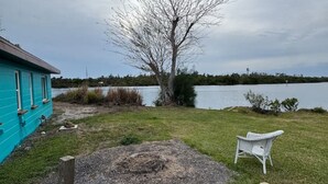 A backyard with a blue house, a tree, a pond, and two Adirondack chairs. - Rivers Edge Bungalow (Front side) (Venice)