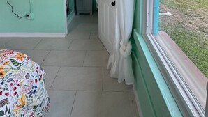 A room with a teal wall, a bed with a floral bedspread, a window with white curtains, and a view of a lake. - Rivers Edge Bungalow (Front side) (Venice)
