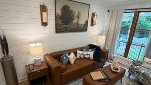 Ein Wohnzimmer mit braunem Sofa, Couchtisch, Teppich und einem Gemälde an der Wand.