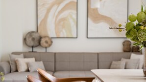 Un comedor con sillas de madera y una mesa, un sofá al fondo, y una obra de arte en la pared.