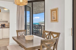 A dining area with a wooden table and chairs, a bowl, a view of the ocean through large glass doors, and a framed picture on the wall.