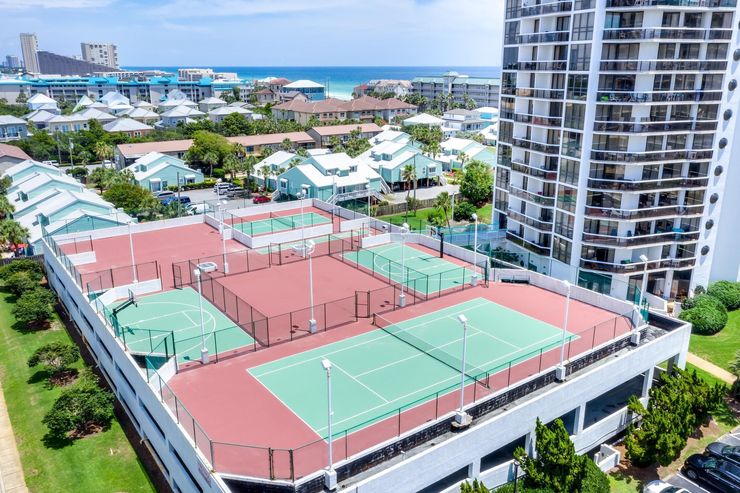 A multi-story building with a rooftop tennis court, surrounded by residential buildings and a view of the ocean.