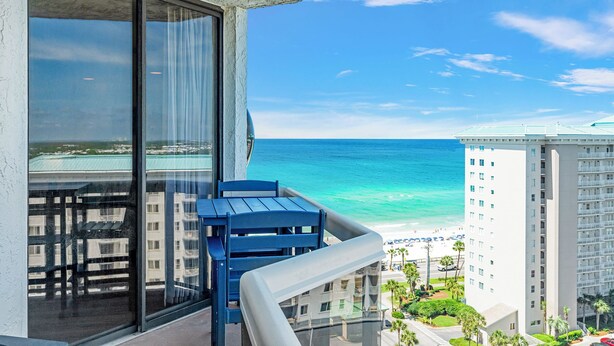 Ein Balkon mit Blick auf das Meer und den Strand, eine Glastür und ein blauer Stuhl.