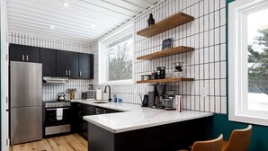 Eine moderne Küche mit schwarzen Schränken, einem Edelstahlkühlschrank, einem Einbauofen, einer großen Kochinsel mit Spüle und Holzregalen über der Arbeitsplatte.