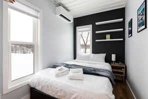 A bedroom with a bed, white towels, a nightstand, a lamp, and a window with a view of trees. - Cargo Cozy - countryside cottage with hot tub (Suttons Bay)