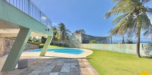Uma piscina de borda curva, cercada por um gramado bem cuidado e palmeiras.