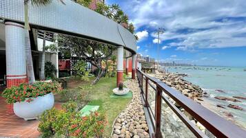 A waterfront promenade with a covered seating area, a view of the sea, and a city skyline in the background.