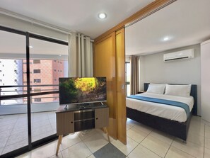 A hotel room with a bed, a TV on a stand, a sliding door, and an air conditioning unit. - Apart-hotel Iate Plaza, Vista Completa da Orla de Fortaleza (Fortaleza)