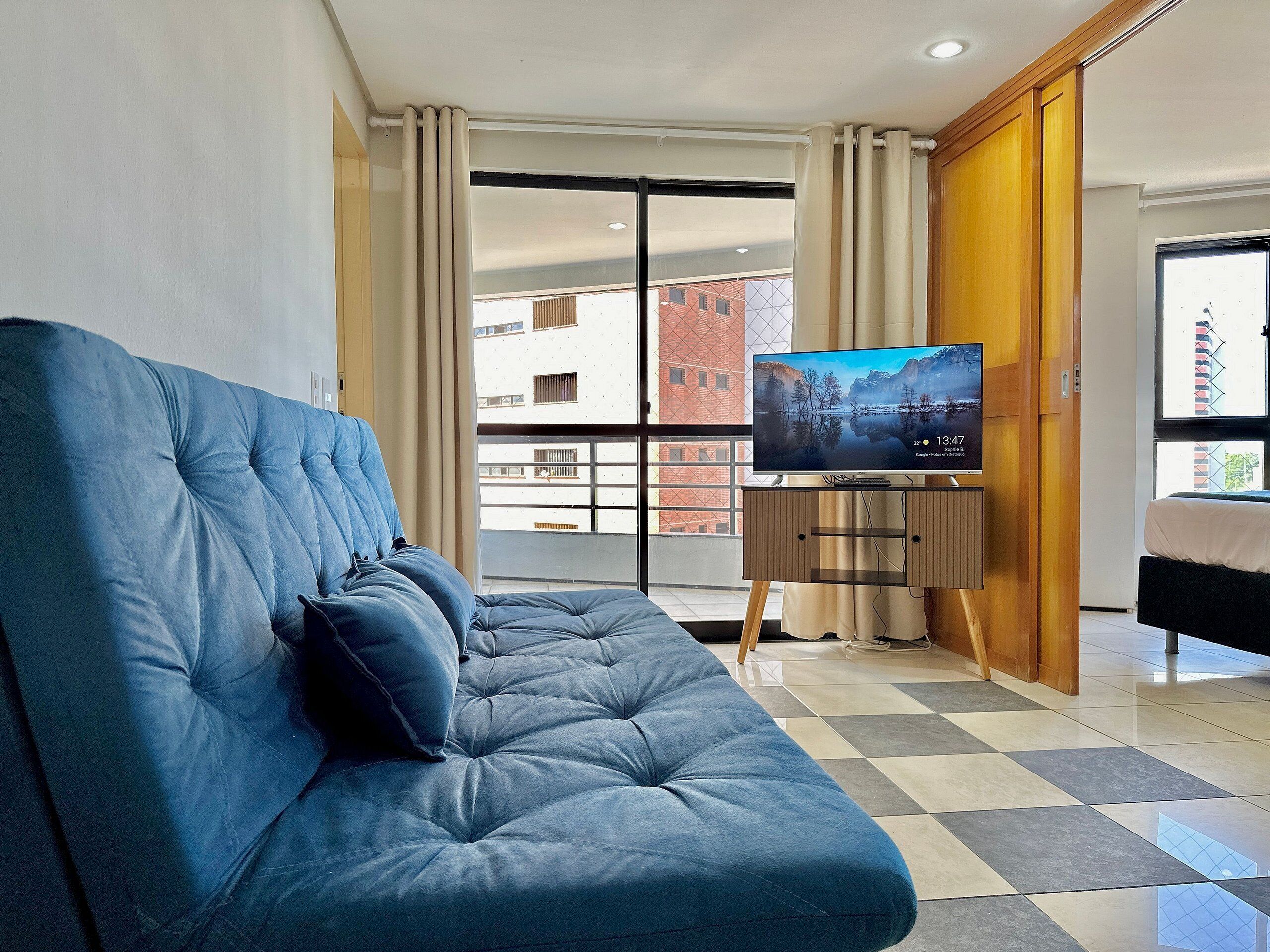 A modern living room with a blue sofa, a television on a stand, and a view of a building through a glass door.