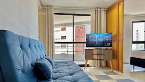 Ett modernt vardagsrum med en blå soffa, en tv på ett tv-bord och utsikt över en byggnad genom en glasdörr.