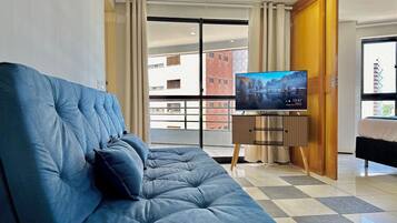 A modern living room with a blue sofa, a television on a stand, and a view of a building through a glass door.