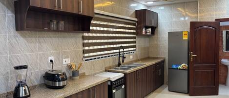 A modern kitchen with dark wooden cabinets, a granite countertop, a built-in oven, and a refrigerator.