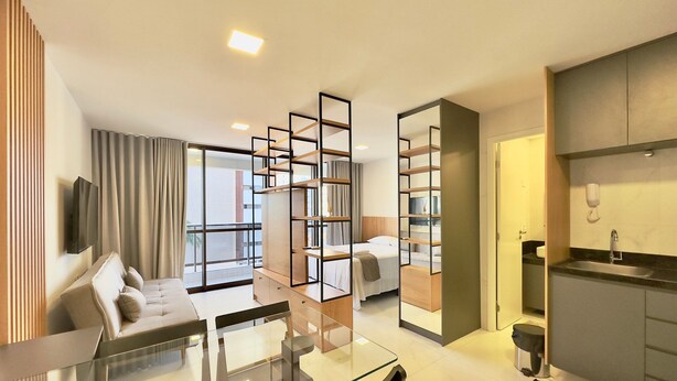 Une chambre d’hôtel moderne dotée d’une table à manger en verre, d’un canapé, d’une télévision, d’un coin cuisine et d’une grande fenêtre.
