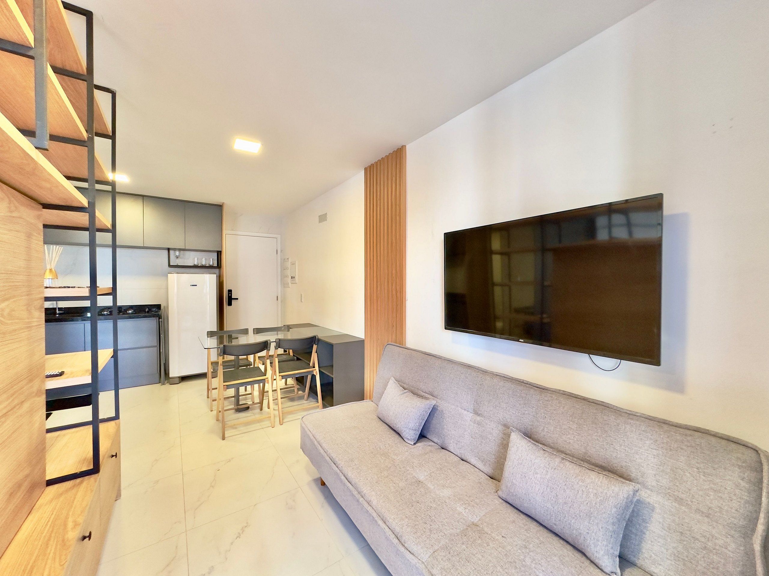 Ein modernes Wohnzimmer mit einer Couch, einem an der Wand befestigten Fernseher und einer Küche im Hintergrund.