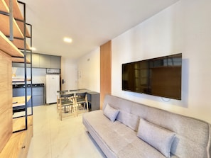 A modern living room with a sofa, a TV mounted on the wall, and a kitchen in the background. - Jsmart - Carolina Sucupira (Fortaleza)