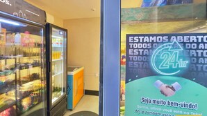 A hotel entrance with a beverage refrigerator stocked with various drinks, a sign indicating 24-hour availability, and a welcoming message. - Jsmart Dom (Fortaleza)