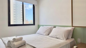 A hotel room with a bed, pillows, a window, and a bedside table with a phone. - Jsmart Dom (Fortaleza)