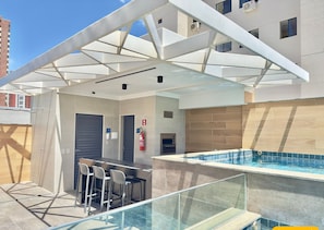 A rooftop pool area with a glass balustrade, a bar with stools, and a covered seating area. - Jsmart Dom (Fortaleza)