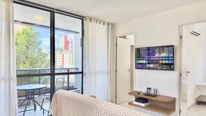 A modern living room with a large window, a sofa, a TV mounted on the wall, and a small table with a remote control. - Jsmart Dom (Fortaleza)