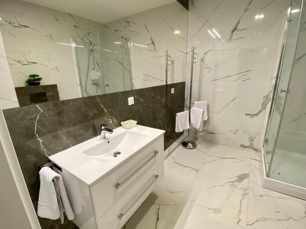 Een moderne badkamer met een glazen douche, marmeren wanden en een witte wastafel.
