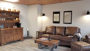 Ein Wohnzimmer mit braunem Ledersofa, einem Holzschrank mit Glaswaren und zwei Wandleuchten.