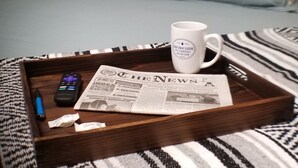 Ein ordentlich bezogenes Bett mit hellblauem Bettzeug, ein Tablett mit einer Zeitung, einer Tasse und einer Fernbedienung auf einem gemusterten Teppich.