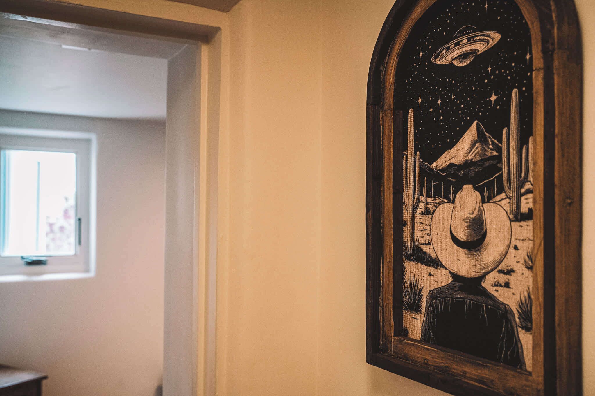 A hallway with a framed artwork depicting a person in a hat, a mountain, and a UFO.