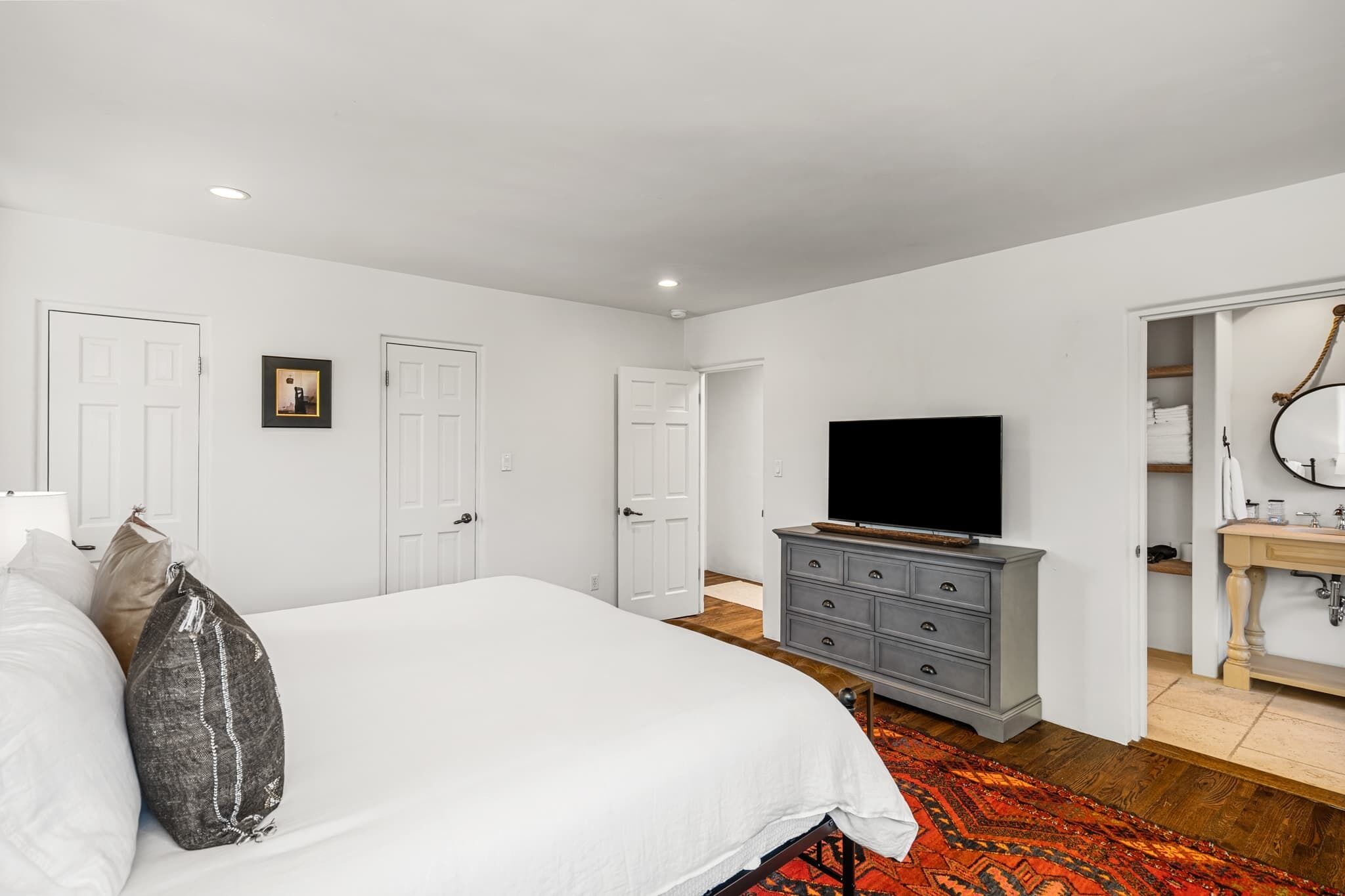 A bedroom with a bed, a dresser, a television, and a bathroom visible through an open door.