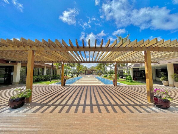 Une allée couverte avec une piscine, une pergola en bois et des plantes en pot.