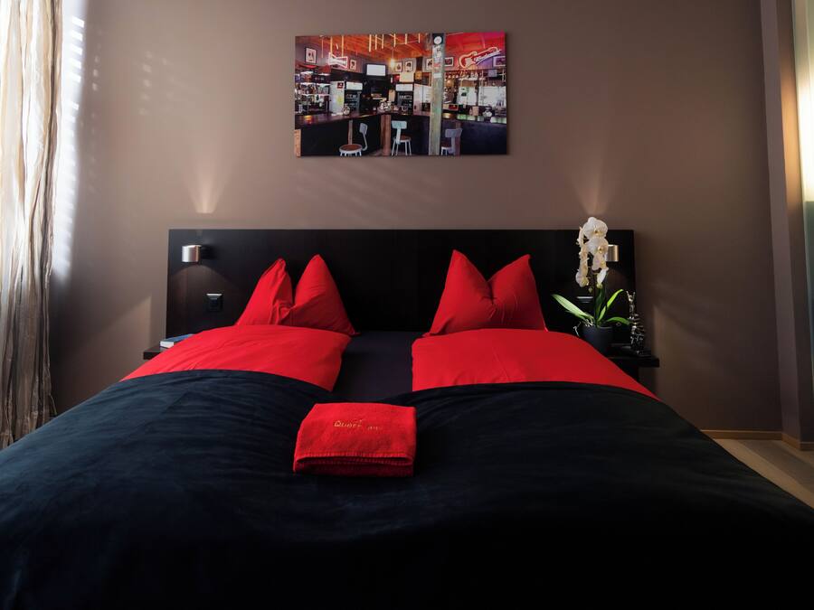 A bed with red and black bedding, a wall-mounted artwork, and a nightstand with a potted plant.