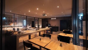Ein modernes Restaurant mit einer langen Theke, mehreren Tischen und einer im Hintergrund sichtbaren Küche.