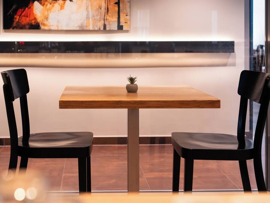 Ein moderner Essbereich mit einem Holztisch, zwei schwarzen Stühlen und einem kleinen Blumentopf.