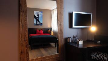 Ein Schlafzimmer mit einem Bett, einem Fernseher, einem spiegelnden Rahmen aus Holz und einem Bild der Golden Gate Bridge.