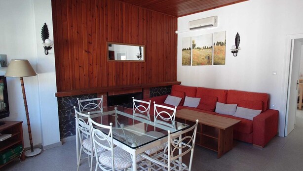 Un coin repas avec une table à plateau de verre et des chaises blanches, un canapé rouge et une cheminée en pierre.