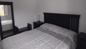 Une chambre à coucher avec un lit, une table de chevet, un miroir et une fenêtre.