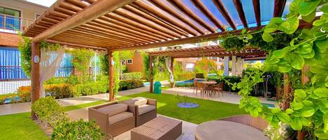 Un espace extérieur abrité, aménagé avec des meubles en osier, une petite piscine et de la verdure.