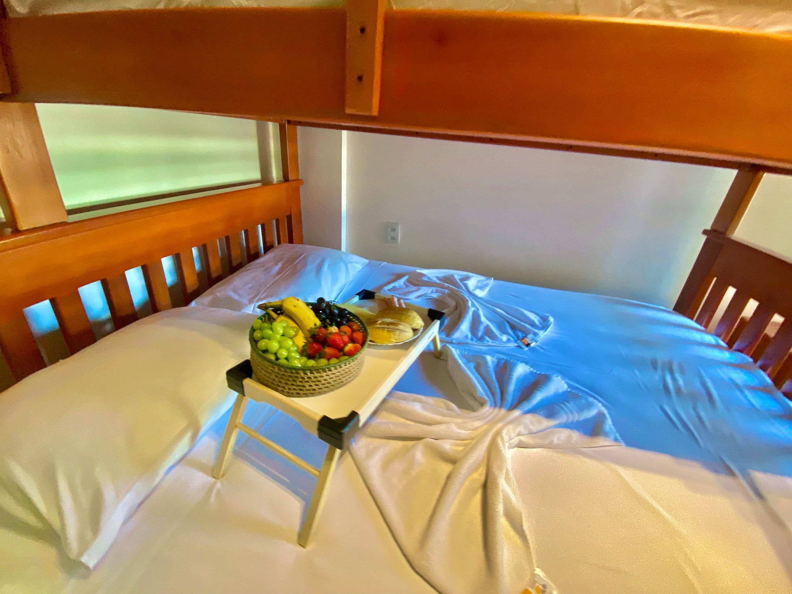 A bunk bed with a wooden headboard, a white mattress, and a tray with fruits and a plate of food.