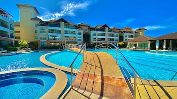 Uma piscina de resort com design curvo, rodeada por edifícios com varandas.