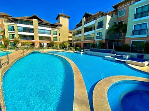 A large outdoor swimming pool surrounded by multi-story buildings with balconies and windows. - Condominio Mediterranee Residence por Be My Guest (Aquiraz)