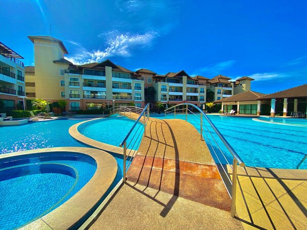 A resort pool with a curved design, surrounded by multi-story buildings with balconies. - Condominio Mediterranee Residence por Be My Guest (Aquiraz)