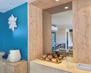 A room with a blue wall, wooden paneling, a white air conditioning unit, a white coffee maker, and a wooden tray with various bowls and glasses.